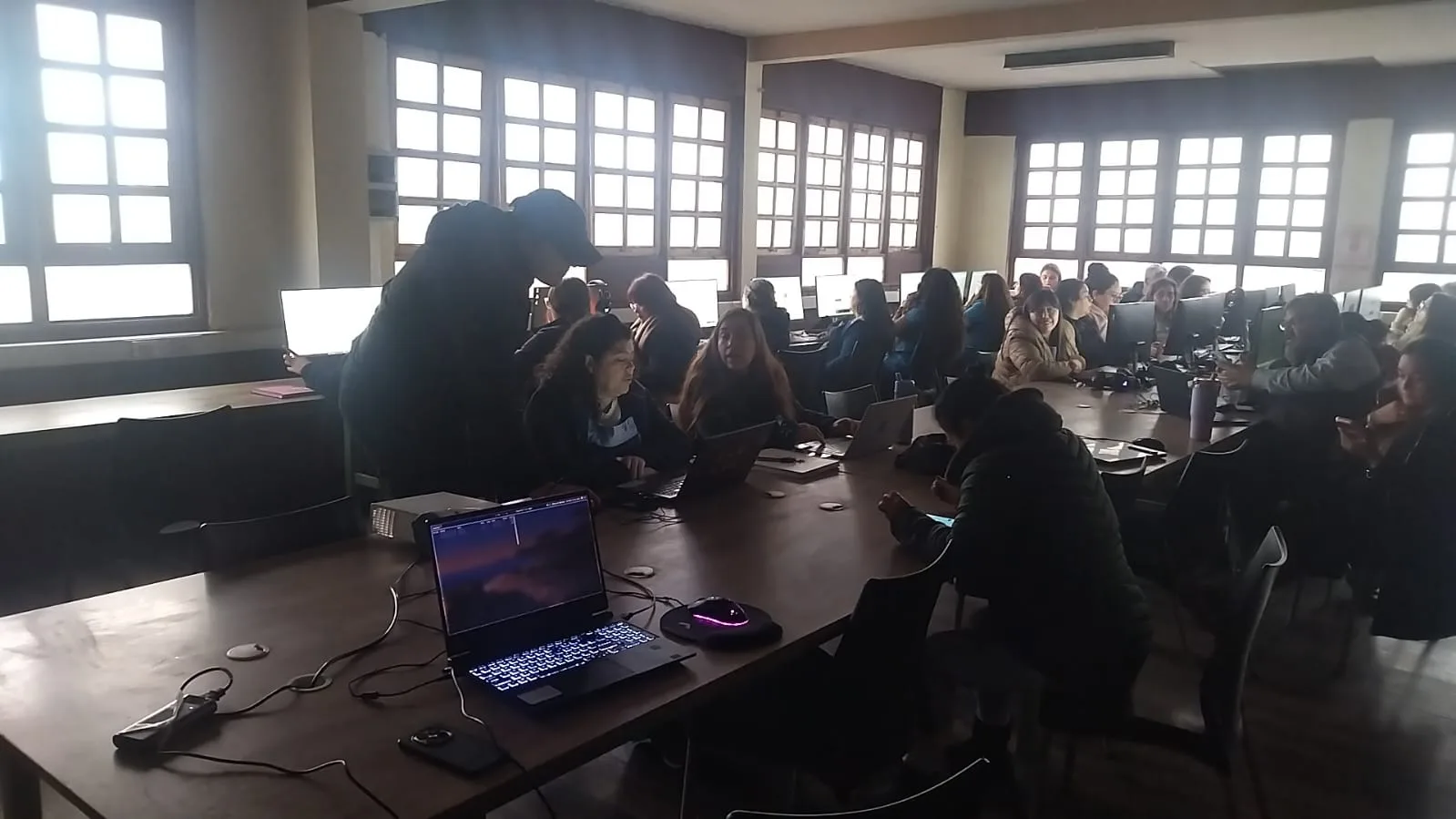 Facilitador acompaña a participantes mientras practican en computadores y teléfonos